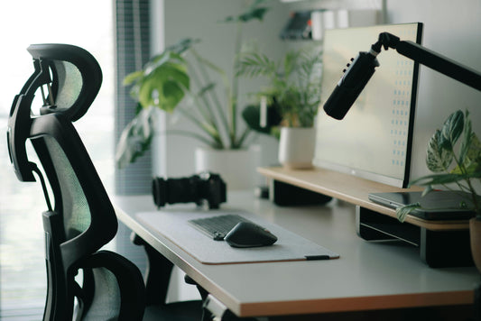 ergonomic chair at a desk with no person. a microphone leaning in and a plant in the background.