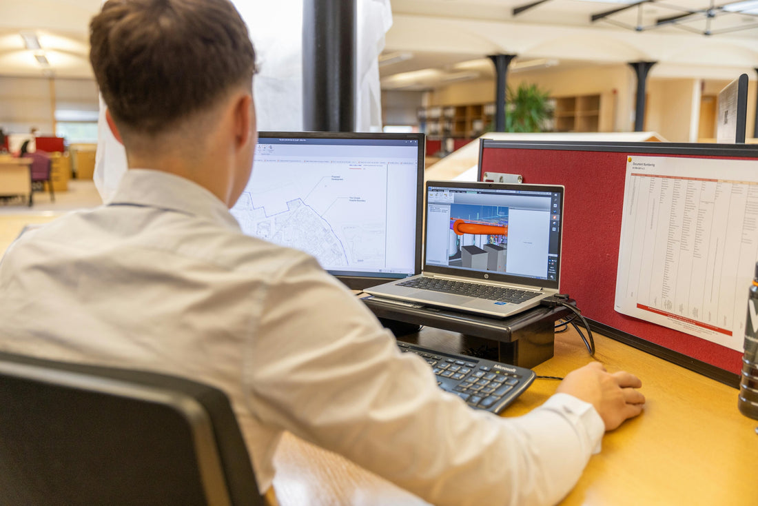 man in a white shirt working at his desk on a raised computer.