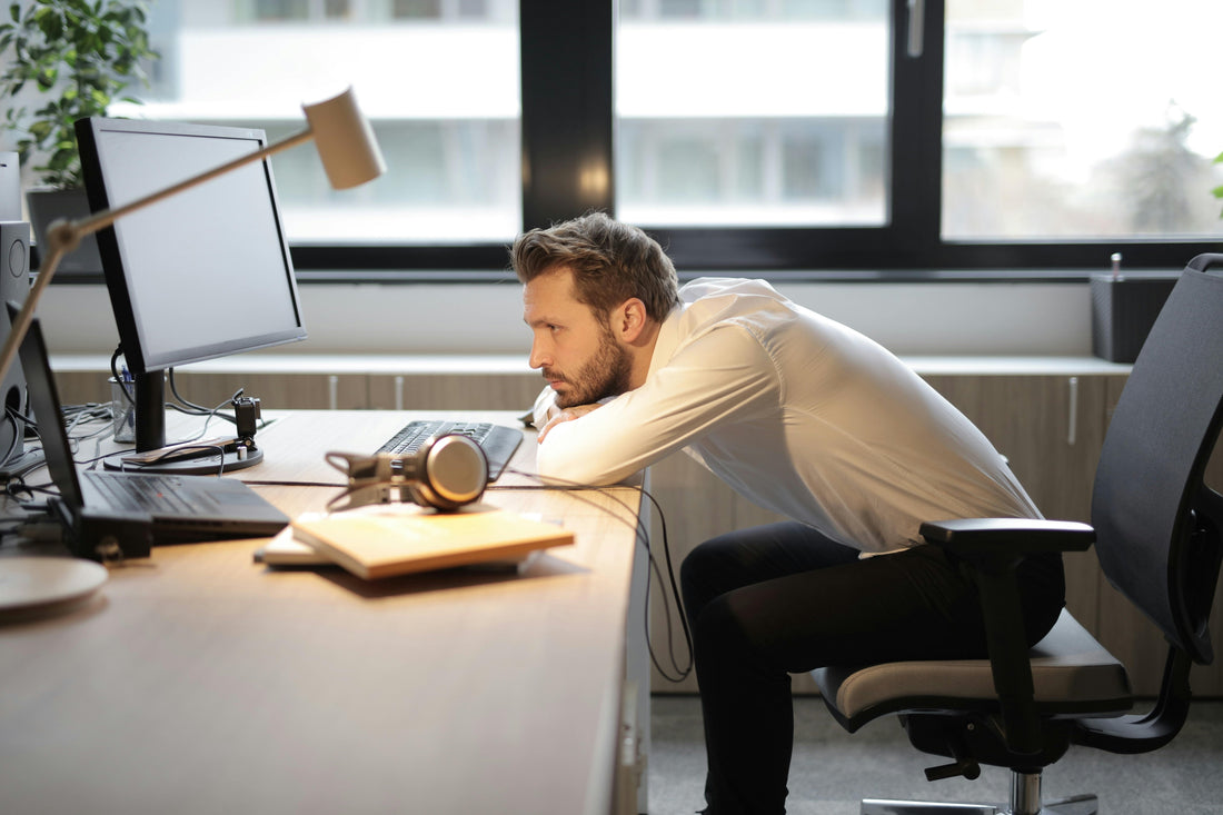 man slouched onto forearms at his office desk.